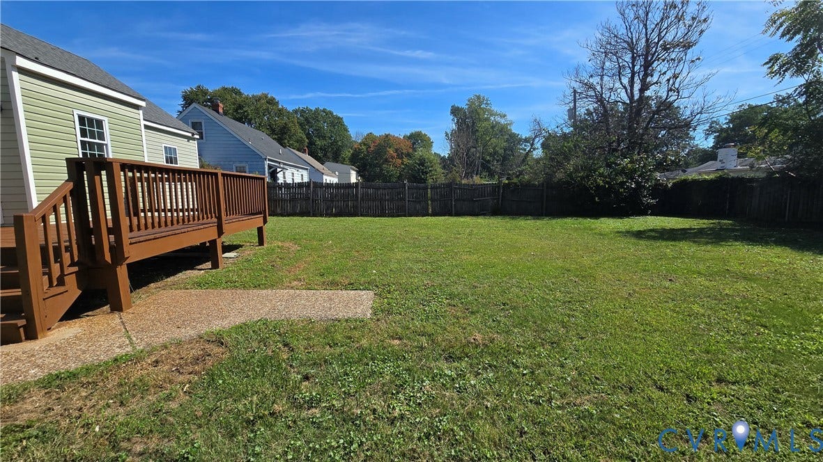 Expansive backyard featuring a manicured lawn, wood privacy fence, and a spacious wood deck with steps