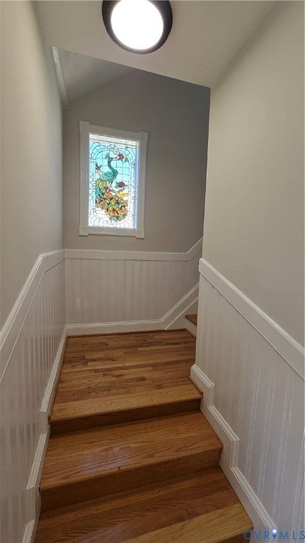 Wood-finish staircase with white paneled wainscoting and a decorative stained glass window