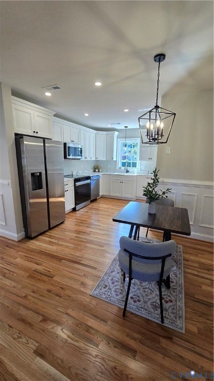 Kitchen featuring wood-finish flooring, white cabinetry, stainless steel appliances, and a geometric pendant light fixture