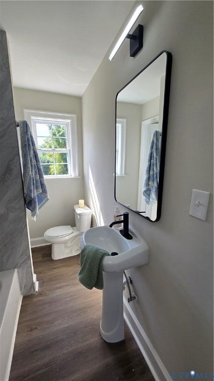 Pedestal sink with a matte black faucet, rectangular wall-mounted mirror, modern linear vanity light, wood-finish flooring, and a window