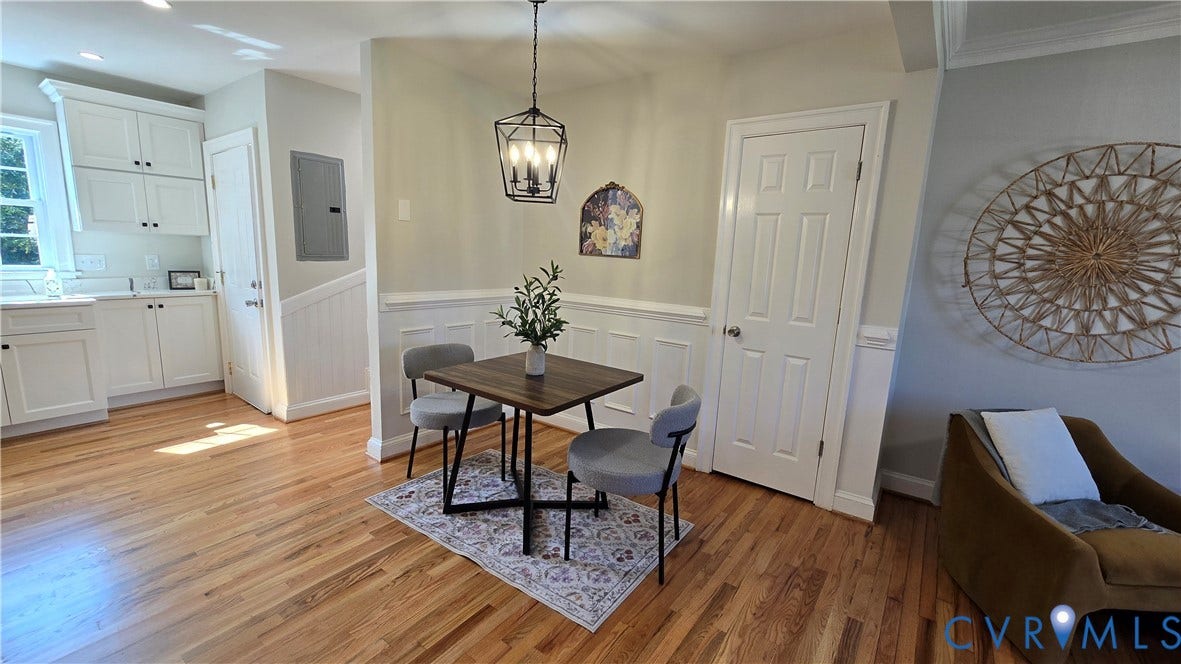 Hardwood flooring throughout, white paneled wainscoting, white kitchen cabinetry, and an open-concept living area with a dark metal light fixture