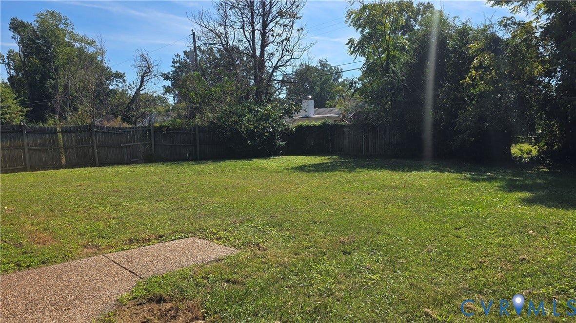 Expansive backyard featuring a lush lawn, mature trees, and a perimeter wood fence
