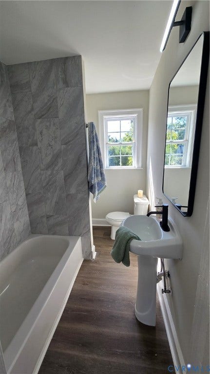 Bathroom featuring a pedestal sink with a matte black faucet, wall-mounted rectangular mirror, and wood-finish flooring