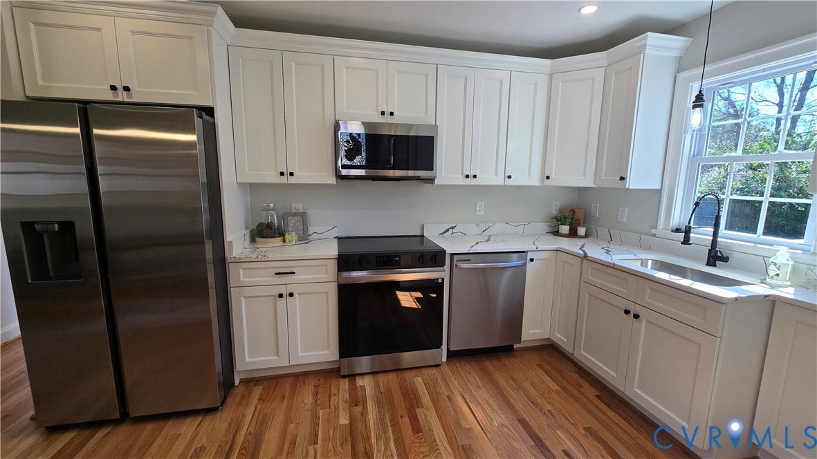 Kitchen featuring white shaker-style cabinetry, stainless steel appliances, wood-finish flooring, and white countertops with a patterned veining