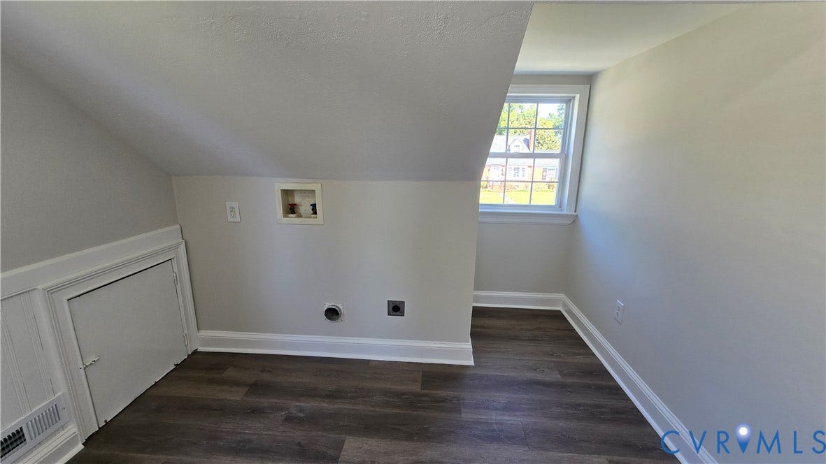 Angled ceiling room featuring wood-finish flooring, a window, and laundry hookups