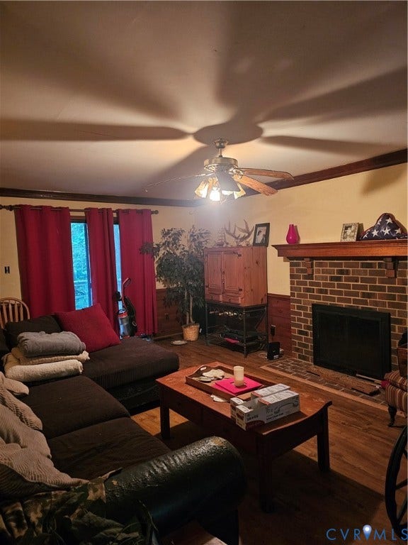Brick fireplace with a wood mantel, wood-finish flooring, wood trim, and a ceiling fan