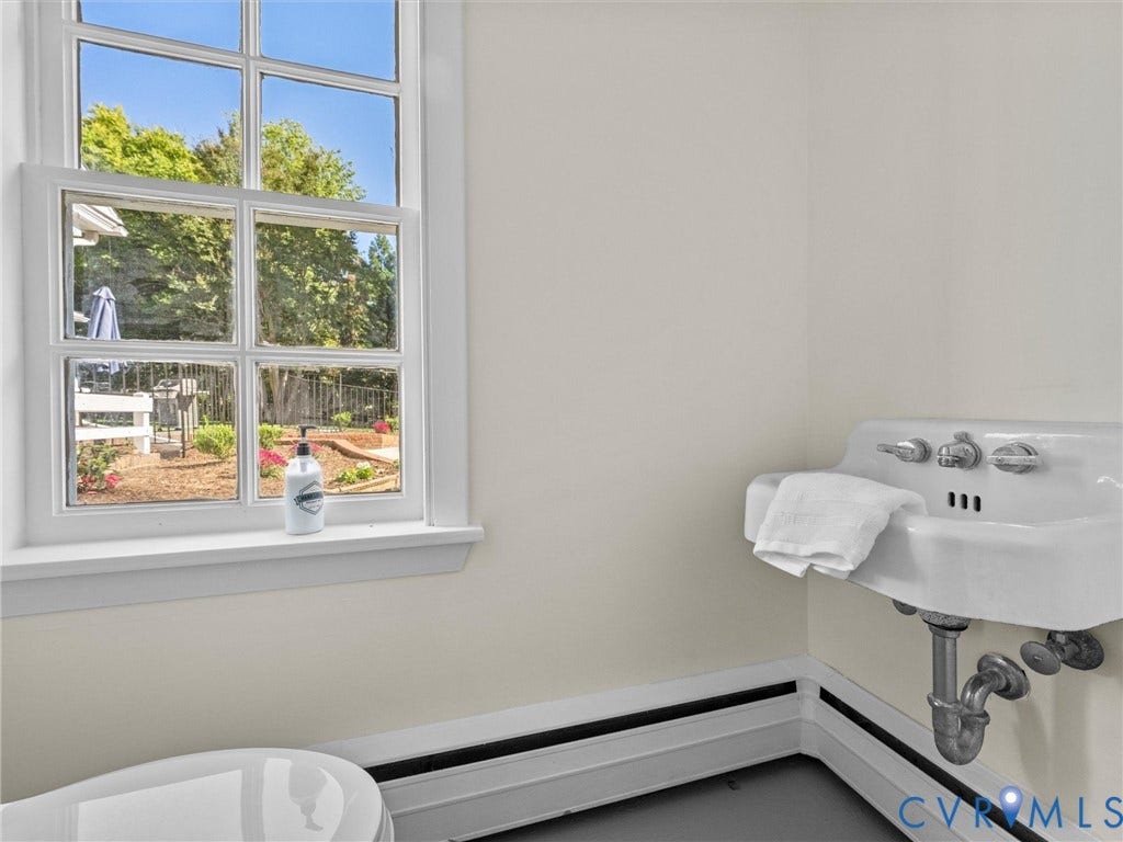 6208 Tapoan Place, Three Chopt, Richmond, VA 23226 Bright, naturally lit bathroom featuring a wall-mounted pedestal sink with chrome fixtures, black wainscoting trim detail, and large multi-pane window overlooking outdoor grounds