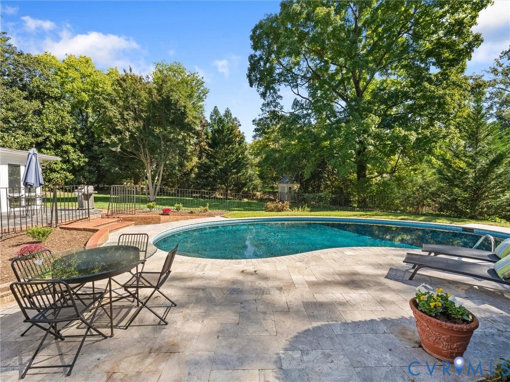 6208 Tapoan Place, Three Chopt, Richmond, VA 23226 Curved swimming pool with surrounding stone tile patio, expansive lawn, mature perimeter trees, and a black wrought iron fence