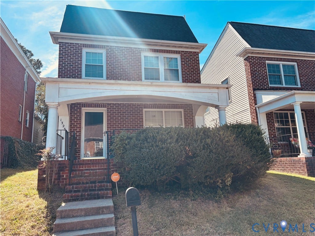 Charming brick colonial featuring a covered front porch with white trim, multi-pane windows, and a two-story design with peaked roofline