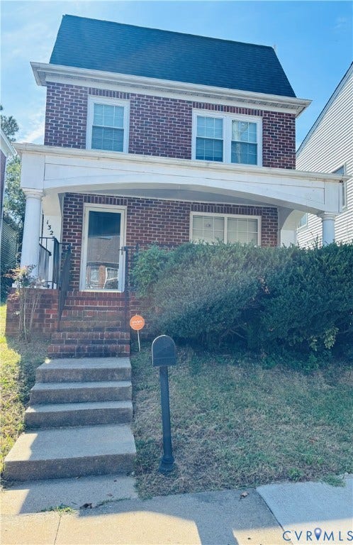 Charming brick Colonial with a two-story facade featuring multipane windows, a pitched roof with blue shingles, and a welcoming front entrance with brick steps and black post-mounted mailbox