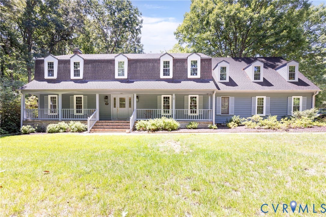 Dormer-style colonial residence featuring a welcoming covered porch, blue siding, a dark shingle roof, and white trim