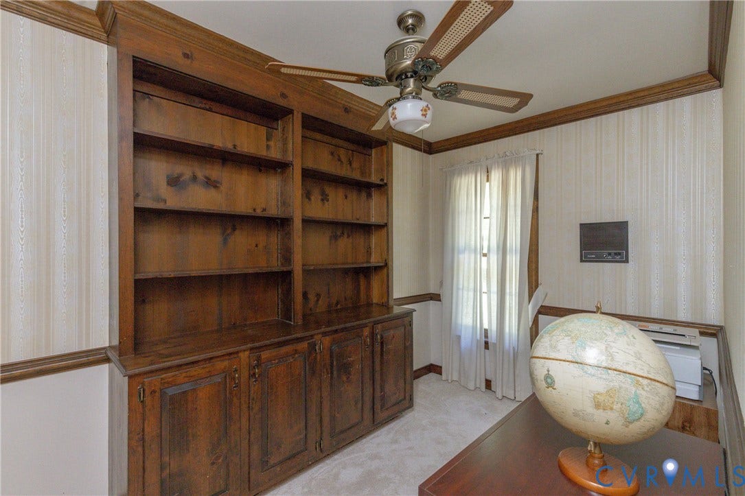Built-in wood-finish cabinetry and shelving, ceiling fan with integrated lighting, window with light-filtering curtains, and striped wall covering
