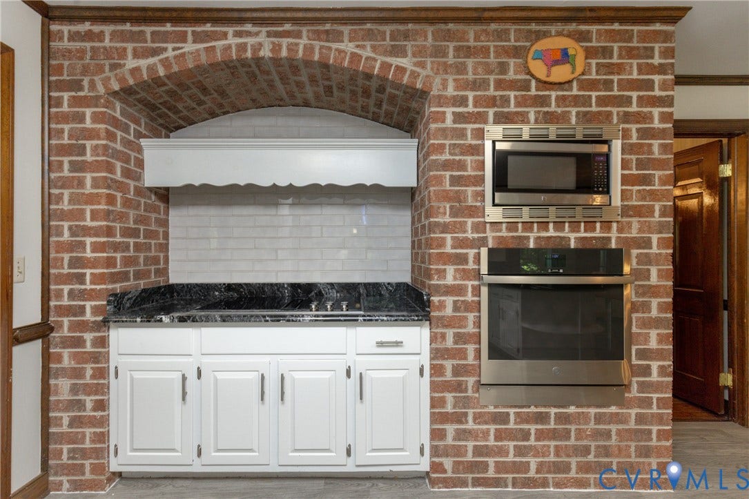 Built-in brick oven enclosure featuring a stainless steel microwave and oven, white cabinetry, dark countertop, and white subway tile backsplash