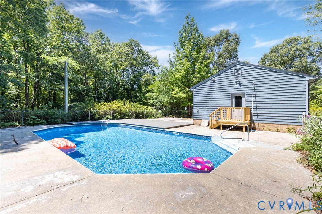 Pool with concrete surround, featuring a light blue siding structure with a wood deck and stairs