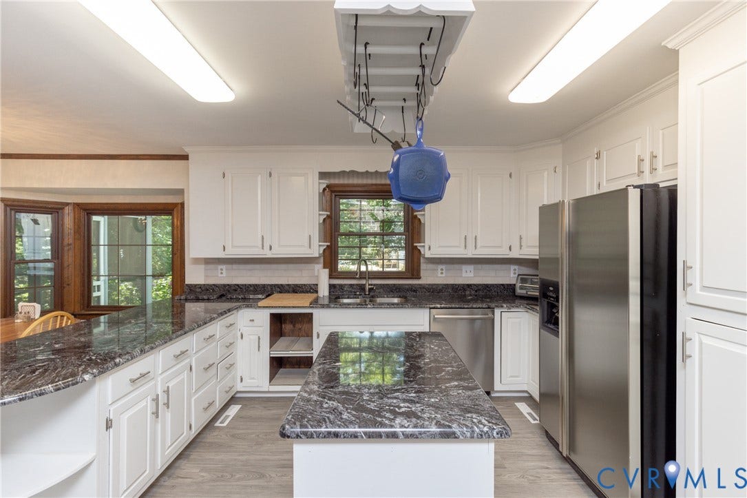 Kitchen featuring white cabinetry, dark stone countertops, stainless steel appliances, wood-finish flooring, and a bay window