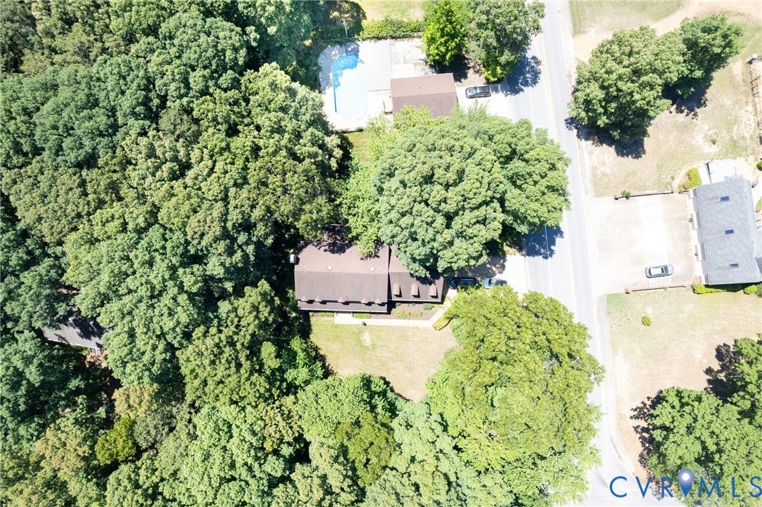 Expansive treed lot featuring a brown shingle roof, paved street frontage, and surrounding mature trees