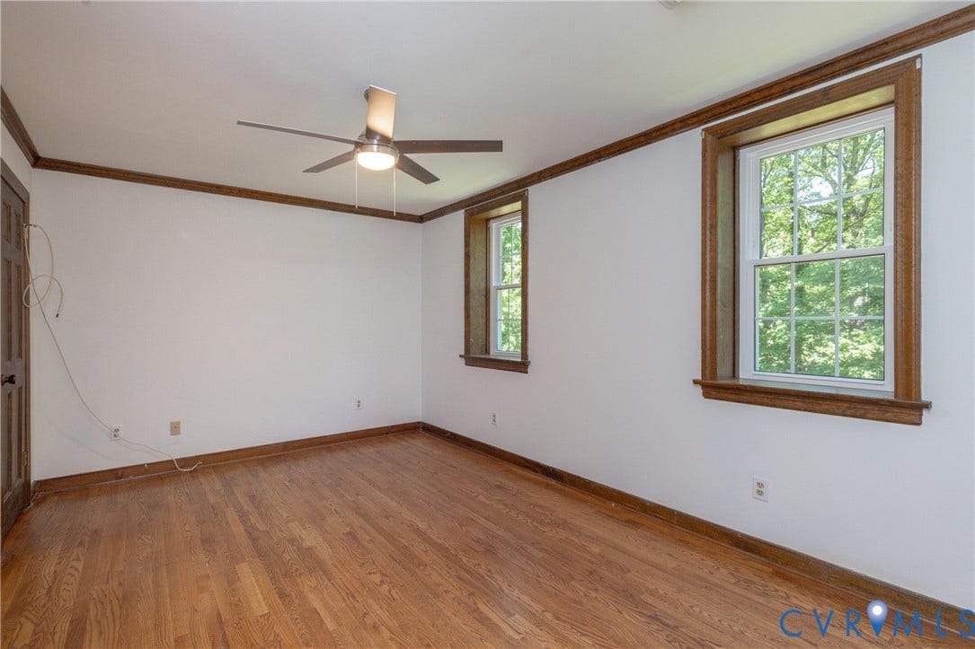 Hardwood flooring throughout, two double-hung windows with wood trim, ceiling fan light fixture, and wood door