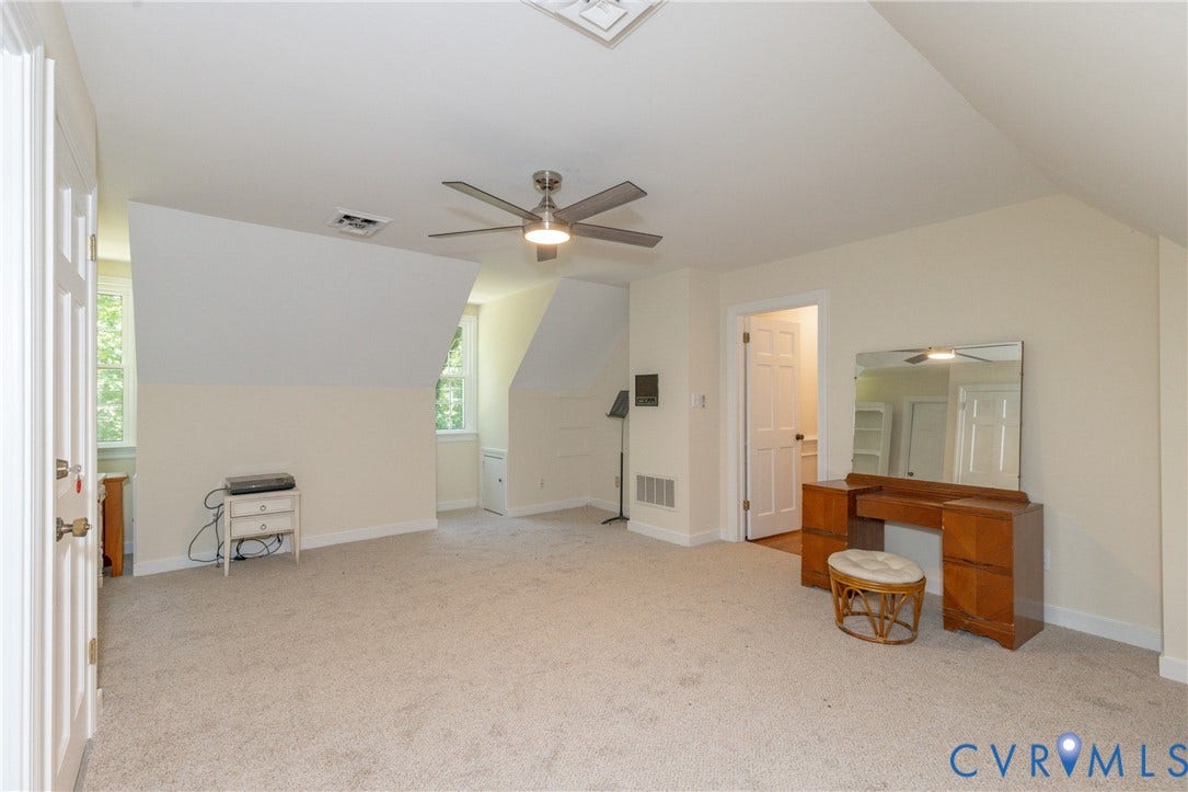 Spacious room with sloped ceilings, light-toned carpeting, and multiple windows