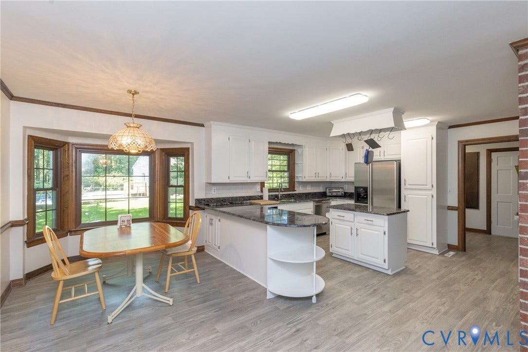 Bay window with wood trim, white cabinetry, dark stone countertops, stainless steel appliances, and wood-finish flooring