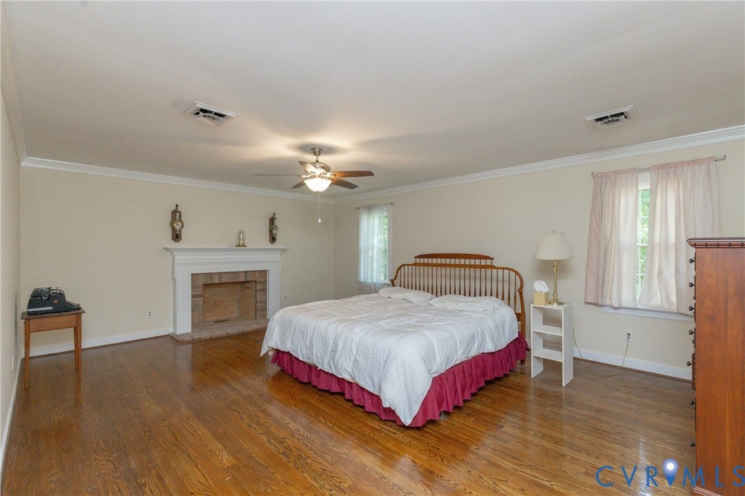 Hardwood flooring, crown molding, brick fireplace with white mantel, ceiling fan, and window with natural light