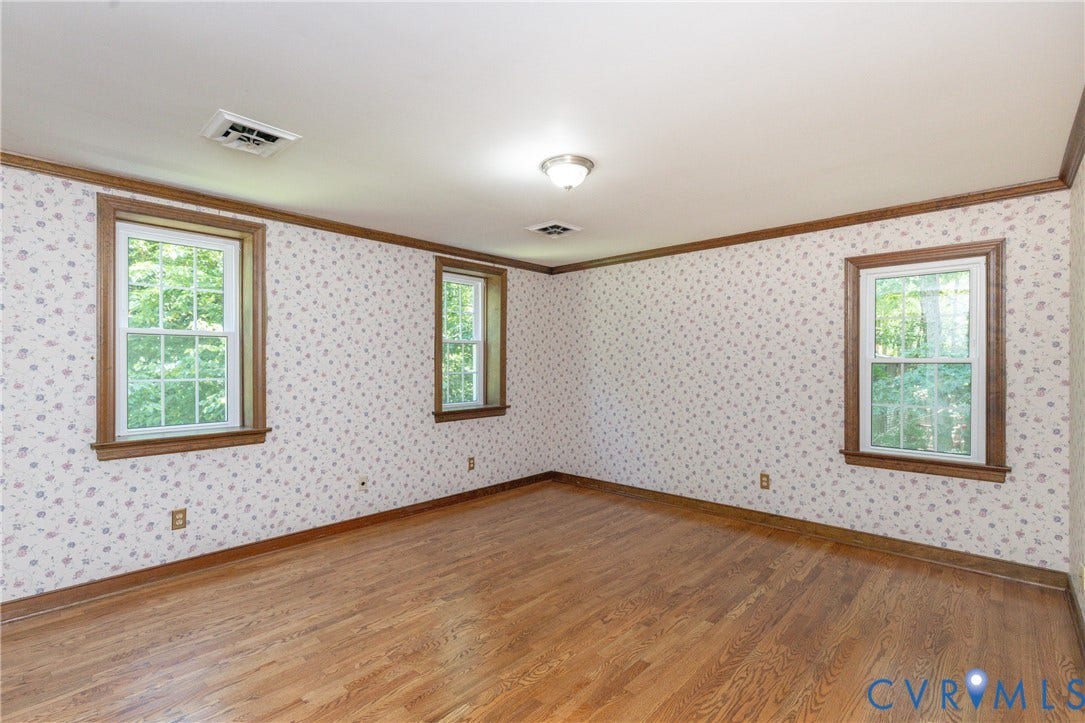 Hardwood flooring, three windows with wood trim, decorative wallpaper, and crown molding
