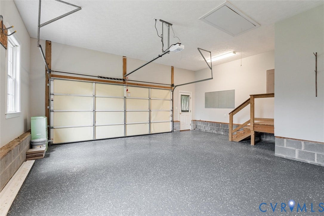 Spacious garage with an overhead door, dedicated access door, interior staircase, and durable flooring