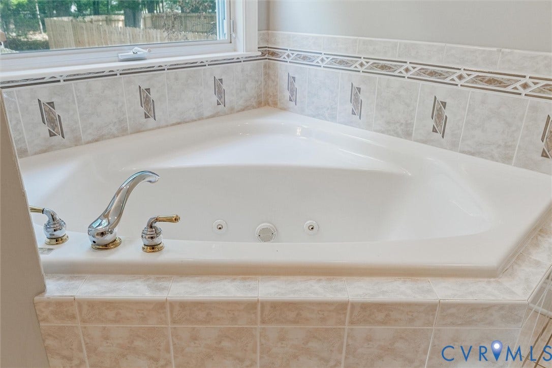 Corner jetted tub with polished chrome and brass fixtures, set within a tiled surround featuring decorative accents