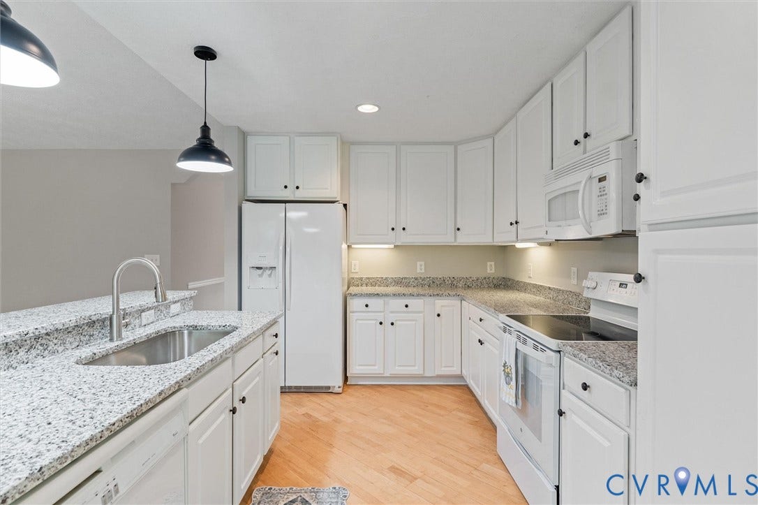 White cabinetry with dark hardware, stone countertops, stainless steel sink with gooseneck faucet, light wood-finish flooring, and pendant lighting fixtures