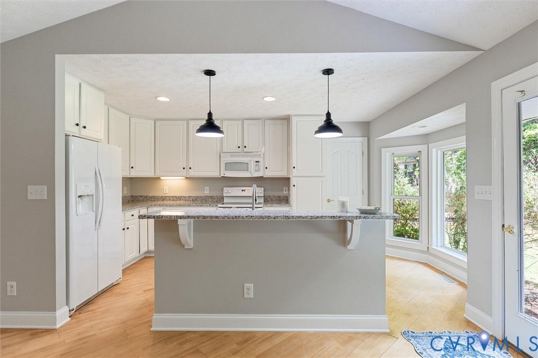 White cabinetry with a granite countertop, wood-finish flooring, white appliances, and a bay window