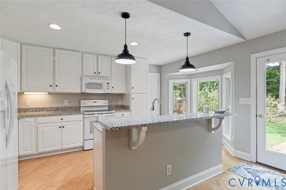 White cabinetry, stone-finish countertops, stainless steel appliances, wood-finish flooring, and a bay window