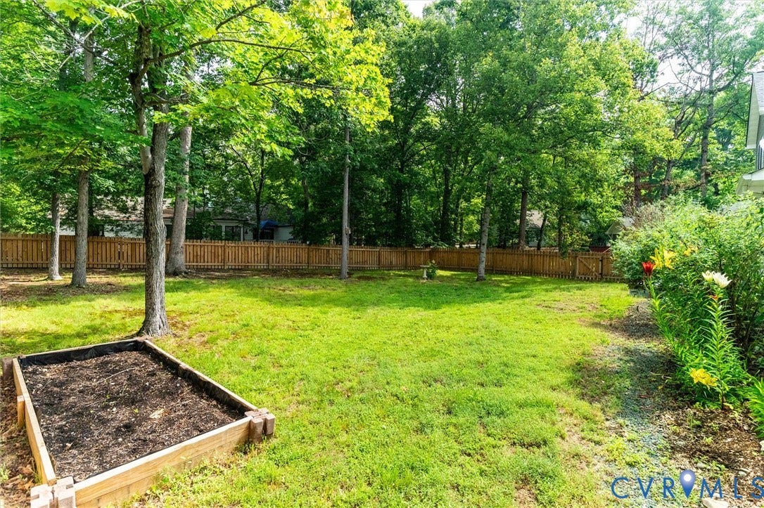 Manicured lawn with a wooden privacy fence, mature trees, a raised garden bed, and a gravel path with planted landscaping