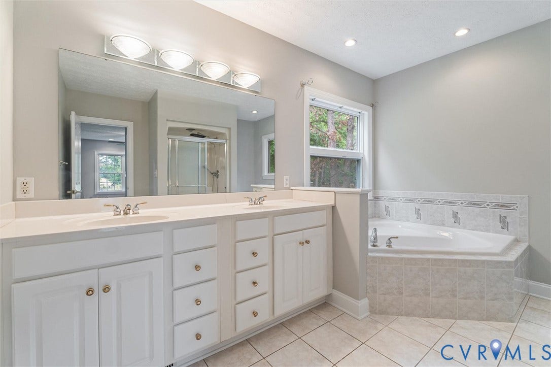 Double vanity with integrated sinks, a built-in corner bathtub, tiled flooring, and a tiled shower enclosure