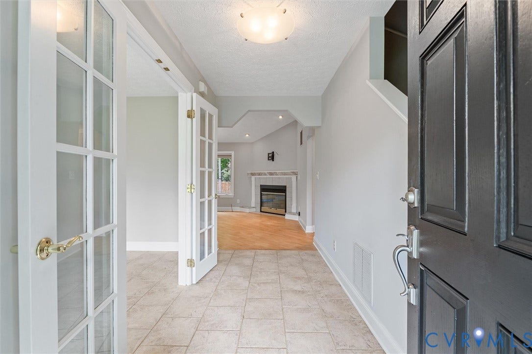 Entryway with tiled flooring, leading to a living area featuring a fireplace with a stone surround