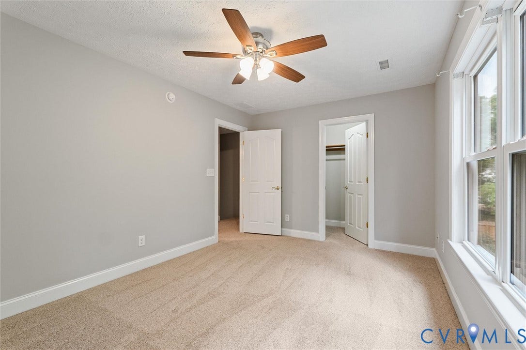 Carpeted room featuring a ceiling fan with light fixture, large window, and two doors
