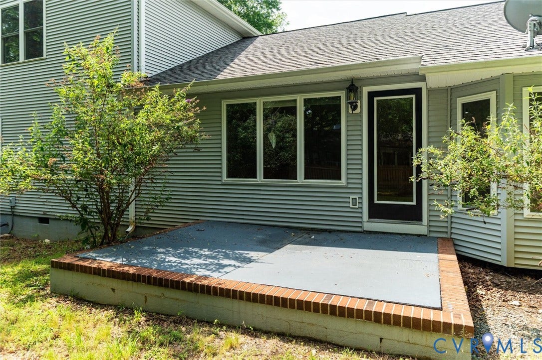 Exterior features include horizontal siding, a patio with brick trim, a dark-framed entry door, and multiple windows