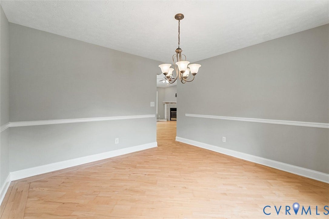 Hardwood-style flooring, light gray wall paint, crown molding, and a bronze-finish chandelier with frosted glass shades
