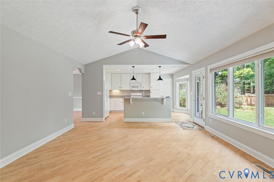 Vaulted ceiling, ceiling fan, wood-finish flooring, white cabinetry, and extensive window-line