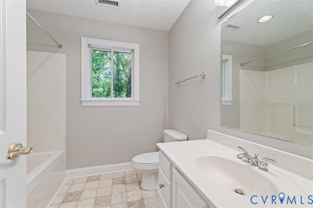 Bathroom featuring a white vanity with integrated sink, chrome faucet, wall-mounted mirror, and a window with white trim