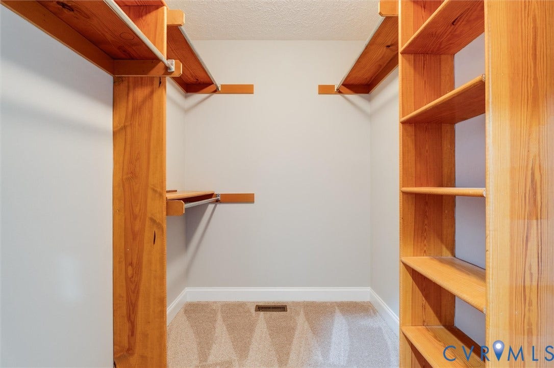 Built-in wood shelving, wood hanging rods, light-toned carpeting, and white baseboards