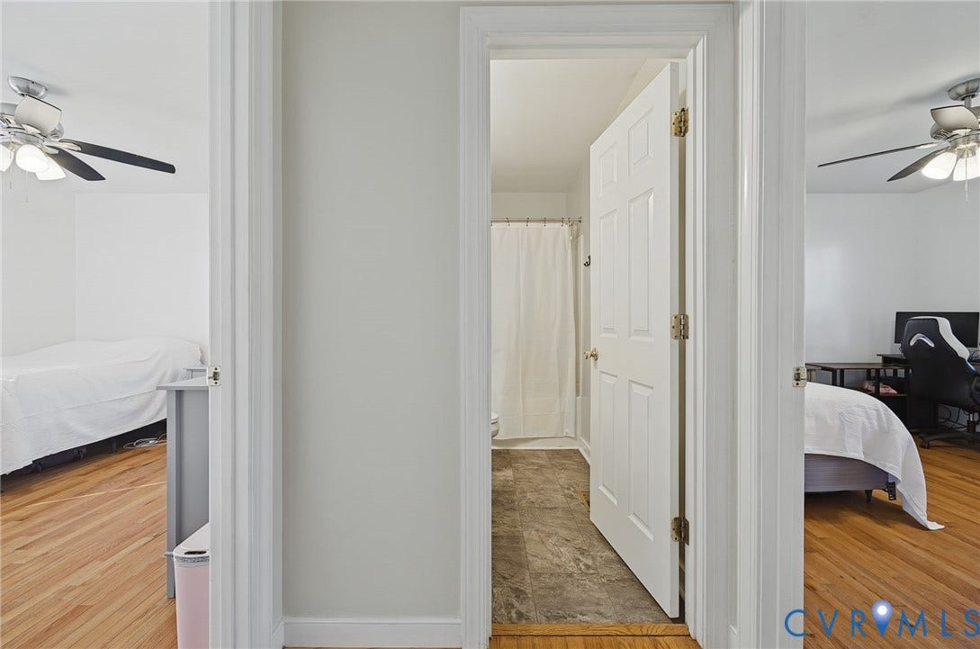 20550 Horseshoe Road, Prince George, VA 23830 Central hallway with wood-finish flooring, leading to a bathroom featuring a shower with a curtain and stone-look tile flooring