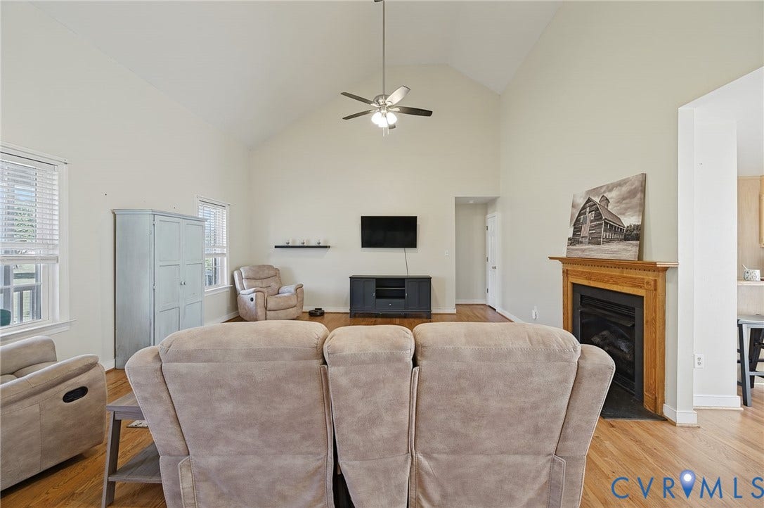 20550 Horseshoe Road, Prince George, VA 23830 Vaulted ceiling with a ceiling fan, wood-finish flooring, natural wood fireplace surround, and multiple windows with blinds