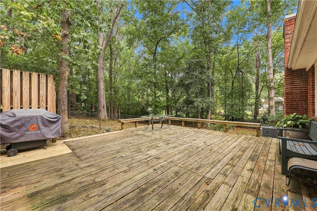 Expansive wood deck with a privacy fence, surrounded by mature trees, and featuring brick exterior siding