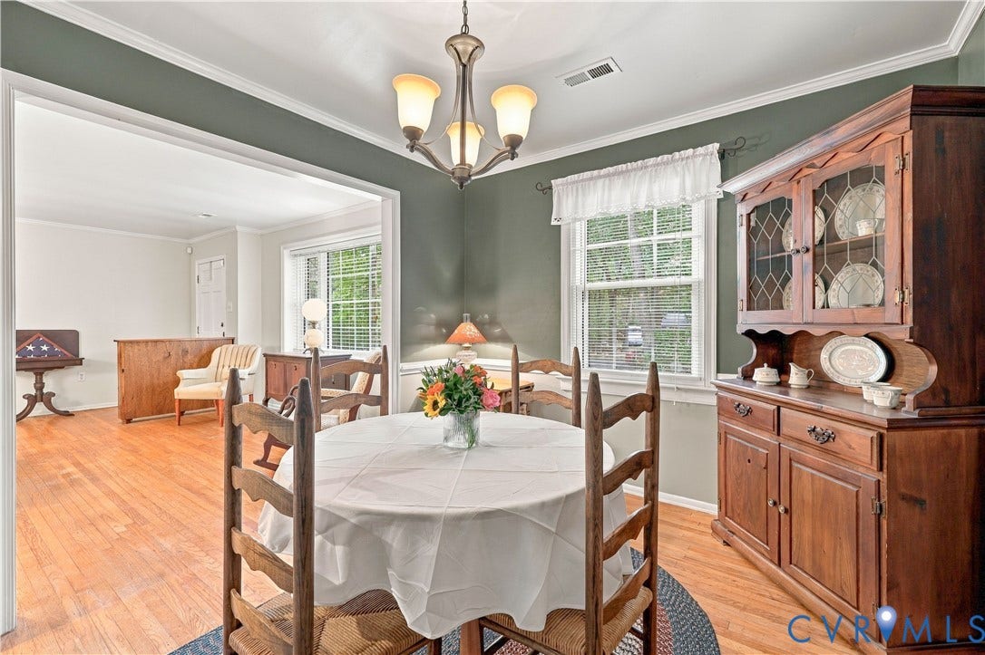 Hardwood flooring, painted accent wall, crown molding, double-hung windows, and a chandelier with glass shades