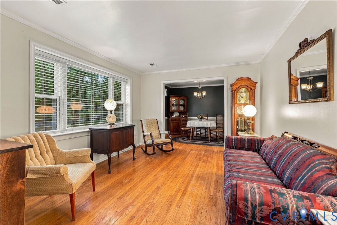 Hardwood flooring throughout, crown molding, large window with blinds, and an arched doorway leading to an additional room