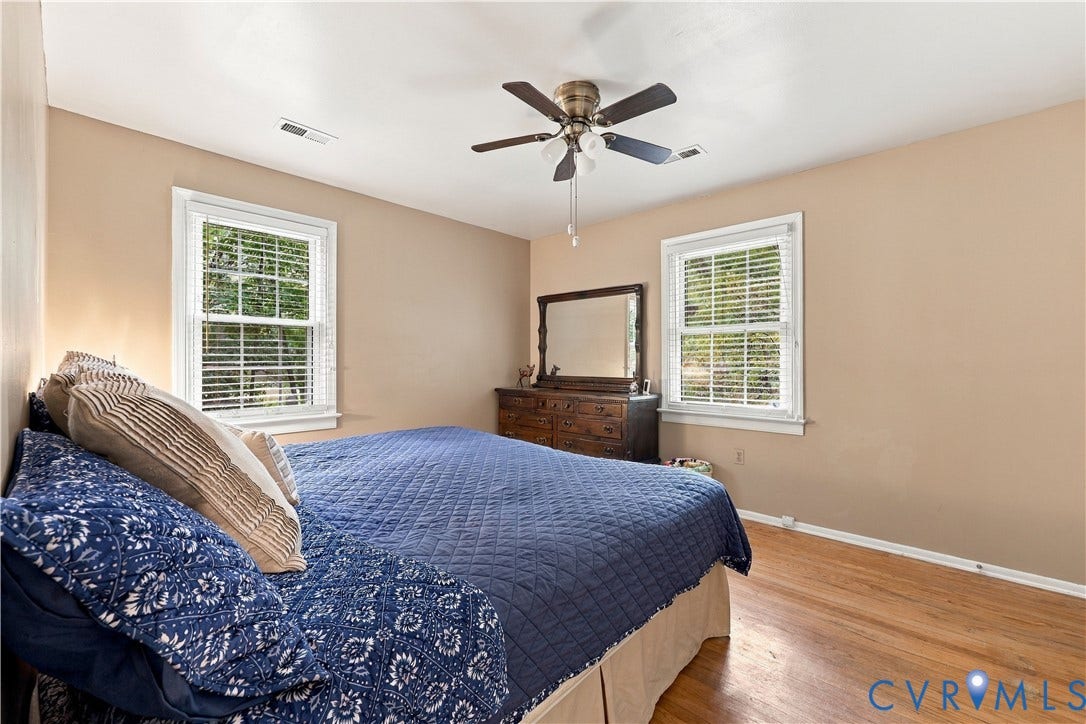 Hardwood-style flooring, dual windows with blinds, and a ceiling fan with light fixture