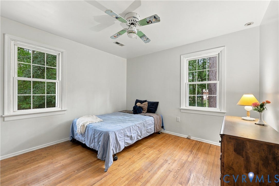 Hardwood flooring, two large windows, white walls, and a ceiling fan