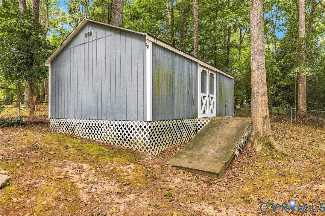Detached storage structure featuring board and batten siding, white double doors, and a built-in access ramp