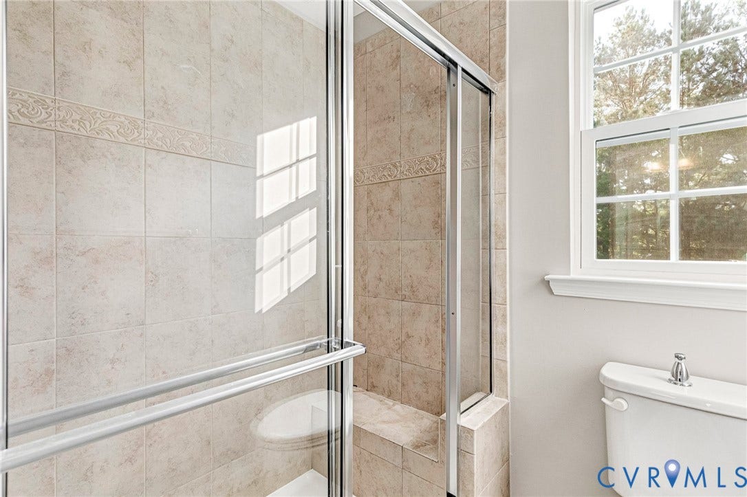 8926 Ringview Drive, Mechanicsville, VA 23116 Shower enclosure with sliding glass doors, a built-in shower bench, and tan tiled walls featuring a decorative band