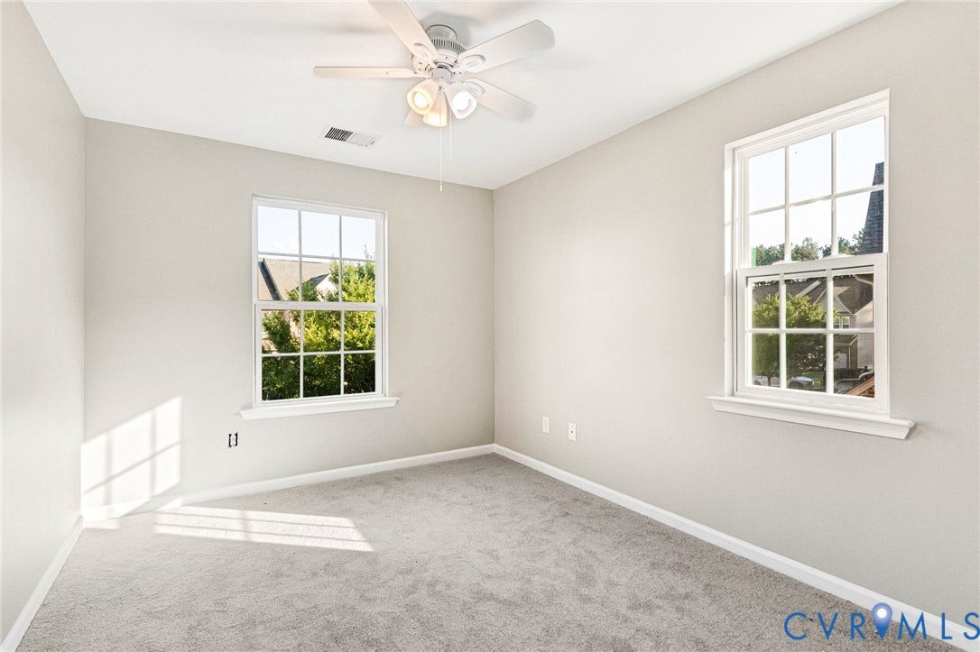 8926 Ringview Drive, Mechanicsville, VA 23116 Light-filled room featuring two windows with grid patterns, a ceiling fan with integrated lighting, and neutral-toned carpeting