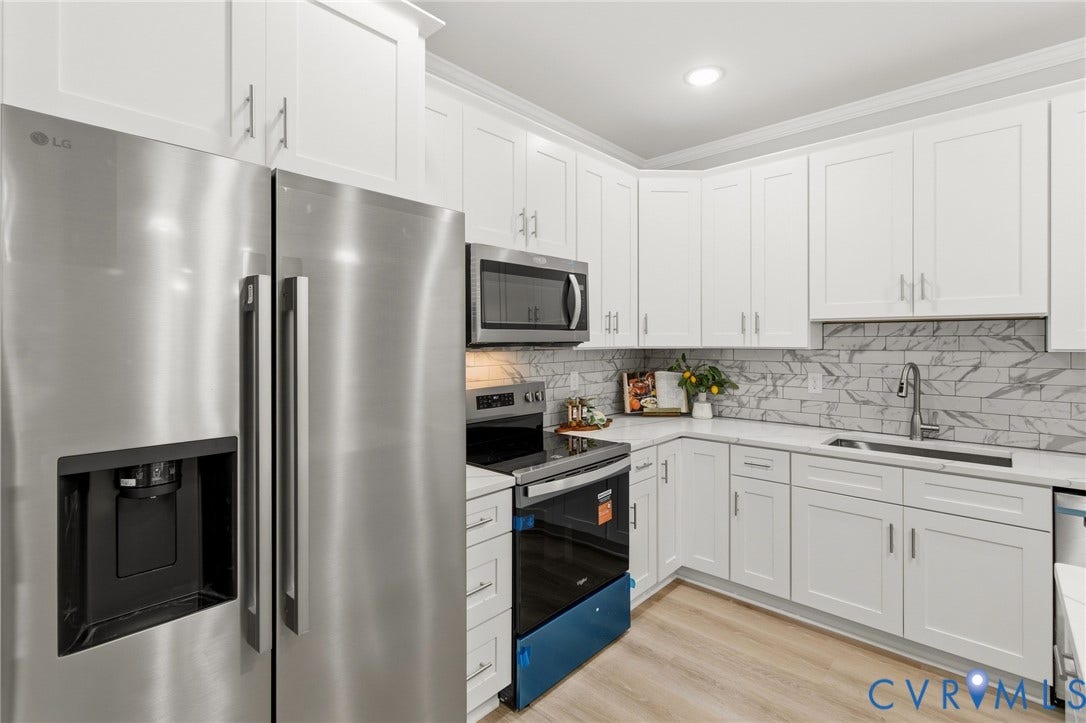 White shaker-style cabinetry with brushed nickel hardware, stainless steel appliances, marble-look tile backsplash, light-toned wood-finish flooring, and solid surface countertops